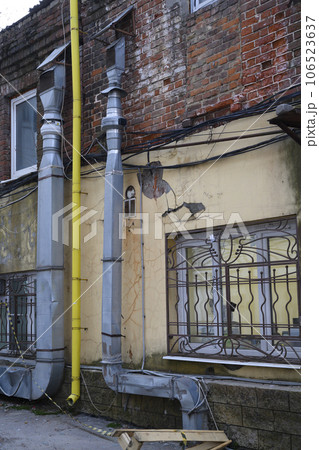 Urban landscape with a brick peeling wall with barred windows, ventilation ducts and yellow gas pipe 106523637