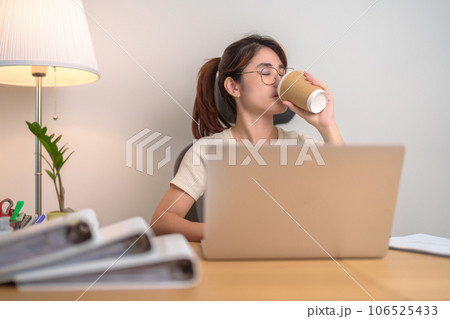 Stressed Asian woman drinking Coffee while working, female businesswoman using laptop with tired and sleepy at office, Exhausted woman with computer at home late night. Overload and Overworked 106525433