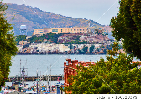 Zoomed in view of Alcatraz Island between trees with distant mountain and boats docked in bay Zoomed in view of Alcatraz Island between trees with distant mountain and boats docked in bay 106528379
