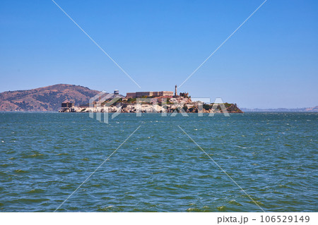 Alcatraz Island on bright summer day with distant mountainous hill and choppy bay waters 106529149