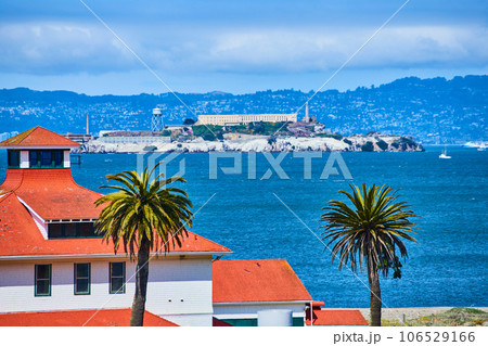 Orange tile roof with palm trees close up and Alcatraz Island in distance with a city on a hill 106529166
