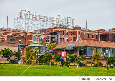 Ghirardelli sign over large red brick building structure in San Francisco with men walking dog 106529178