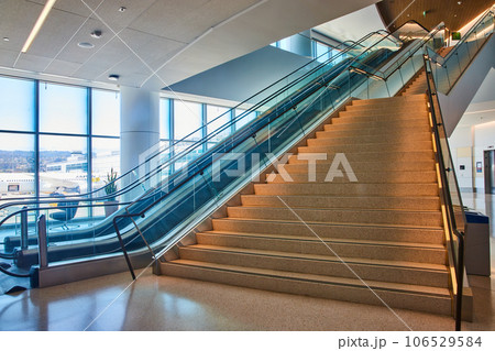 Bottom to top view of generic stairs ascending with two escalators on left side and distant elevator 106529584
