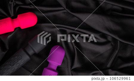 Three colored dildos on a black silk sheet.  106529961