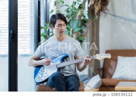 自宅でギターの練習をする若い男性 106530112