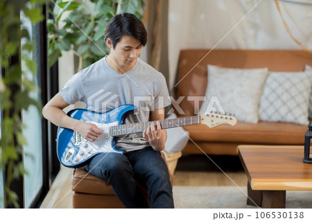 自宅でギターの練習をする若い男性 106530138