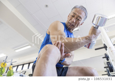 トレーニングジムでダンベルを使って筋トレをする中高年男性　コンセントレーションカール 106531031