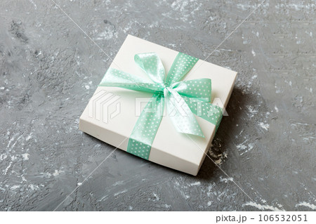wrapped Christmas or other holiday handmade present in white paper with green ribbon on colored background. Present box, decoration of gift on colored table, top view with copy space 106532051