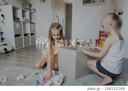 Children cleaning toys from floor after playing, collect them to textile box. Kids sitting on carpet at white home bedroom, kindergarten playroom or playground center. Educational eco-friendly games 106532266