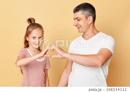 Cute smiling brwon haired little girl standing with her father and making heart shape with hands together expressing love family realtionship. Cute smiling brwon haired little girl standing with her father and making heart shape with hands together expressing love family realtionship. 106534112