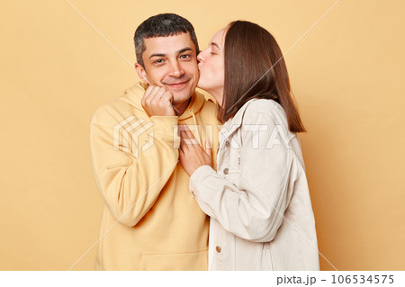 Romantic woman kissing man cheek, family wearing casual style clothing standing isolated over beige background expressing feelings and love. 106534575