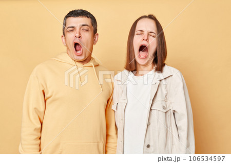 Sleepy tired friends woman and man wearing casual style clothing standing isolated over beige background yawning needs rest, drowsing, having nap. Sleepy tired friends woman and man wearing casual style clothing standing isolated over beige background yawning needs rest, drowsing, having nap. 106534597