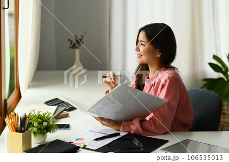 Charming millennial female manager sitting at office desk and looking away, daydreaming or thinking of new business ideas Charming millennial female manager sitting at office desk and looking away, daydreaming or thinking of new business ideas 106535013