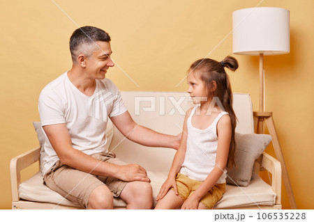 Faily relationship. Happy parenthood. father with child daughter wearing casual clothing sitting on sofa against beige background pleasant conversation. Faily relationship. Happy parenthood. father with child daughter wearing casual clothing sitting on sofa against beige background pleasant conversation. 106535228