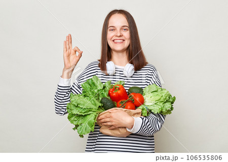 Smiling cheerful woman embraces fresh vegetables posing isolated over white background showing okay sign like to eat organic food looking at camera with happy face. 106535806