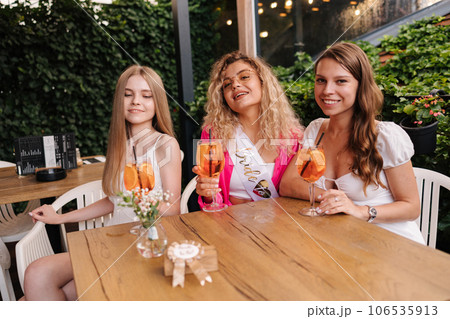 Three girls sits in cafe and drinks cocktails. Happy friends celebrate event together 106535913