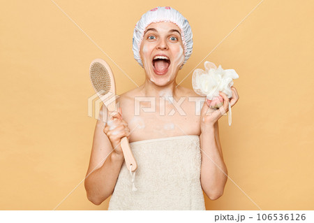 Portrait of beautiful excited amazed woman taking shower in bathroom holding washcloth and body brush for scrub and massage screaming happily enjoying skin care procedures. 106536126