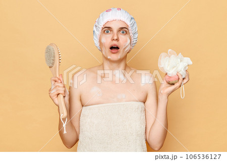 Clean body care. Natural skincare routine. Fresh morning routine. Scared shocked young woman in shower cap and wrapped in towel isolated over beige background. 106536127