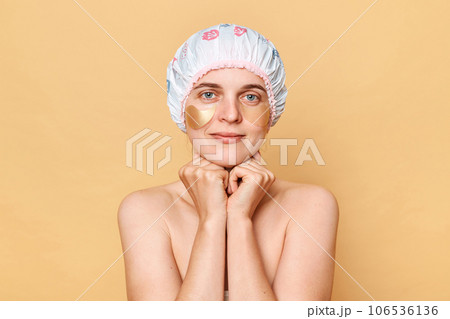 Taking care of her skin. Daily pampering routine. Woman using eye patches spending time for beauty procedures after talking shower, keeps hands under chin, looking at camera. Taking care of her skin. Daily pampering routine. Woman using eye patches spending time for beauty procedures after talking shower, keeps hands under chin, looking at camera. 106536136