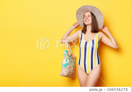 Delighted attractive woman wearing swimsuit isolated on yellow background standing looking away copy space for promotional text advertisement area. Delighted attractive woman wearing swimsuit isolated on yellow background standing looking away copy space for promotional text advertisement area. 106536278