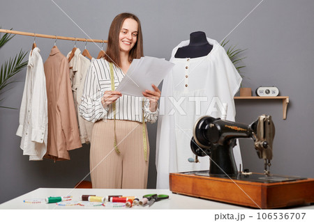 Fashion woman designer making holding papers with sketch in workshop, thinking about new collection, smiling, seamstress creating new outfits. Fashion woman designer making holding papers with sketch in workshop, thinking about new collection, smiling, seamstress creating new outfits. 106536707
