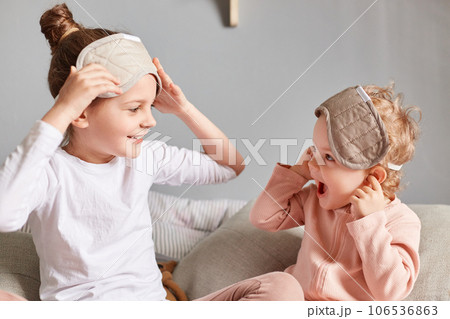 Happy kids sisters spending time together in bedroom, wearing blindfolds on their eyes, laughing and having fun, feeling refreshed and happy, spending their leisure time on the weekend morning. Happy kids sisters spending time together in bedroom, wearing blindfolds on their eyes, laughing and having fun, feeling refreshed and happy, spending their leisure time on the weekend morning. 106536863