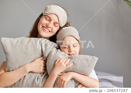 Portrait of mother with her cute little daughter sitting on bed with closed eyes having nap enjoying weekend day drowsiness smiling with happy faces. Portrait of mother with her cute little daughter sitting on bed with closed eyes having nap enjoying weekend day drowsiness smiling with happy faces. 106537287