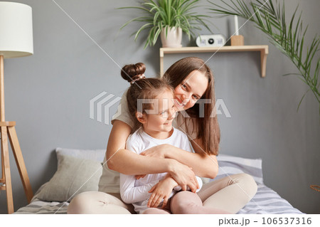 Young girl sitting with her mother in their cozy room, smiling and feeling togetherness of relationship, enjoying leisurely day filled with love and relaxation. 106537316