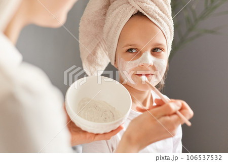 Unrecognizable mother and little daughter posing at home together smiling happy child with cream on face looking smiling at mommy family beauty treatment. 106537532