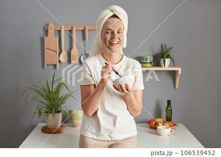 Beautiful caucasian smiling young woman posing in kitchen with towel on head making cosmetology procedures skin care treatment lazy beauty morning. 106539452