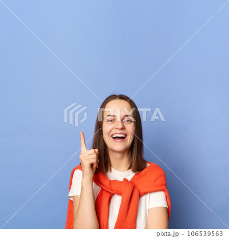 Inspired excited woman wearing white t-shirt and jumper over neck standing isolated over blue background raised finger up has idea pointing at copy space upwards. 106539563