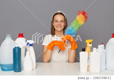 Joyful happy smiling woman posing at workplace with cleaning detergents sitting with pp duster in hands cleaning her house isolated over gray background. Joyful happy smiling woman posing at workplace with cleaning detergents sitting with pp duster in hands cleaning her house isolated over gray background. 106539611