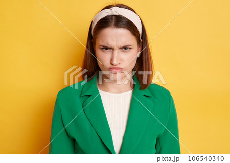 Offended unhappy angry woman wearing green jacket posing isolated over yellow background looking at camera frowning face offended negative feelings. Offended unhappy angry woman wearing green jacket posing isolated over yellow background looking at camera frowning face offended negative feelings. 106540340