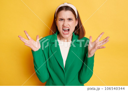Angry irritated woman wearing green jacket posing isolated over yellow background arguing screaming with hate raised her arms yelling with anger. 106540344