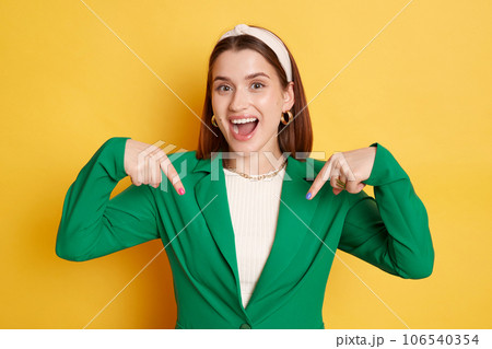 Overjoyed attractive woman wearing green jacket posing isolated over yellow background pointing up asking to subscribe her blog looking at camera with happy face. Overjoyed attractive woman wearing green jacket posing isolated over yellow background pointing up asking to subscribe her blog looking at camera with happy face. 106540354