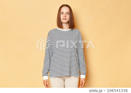 Serious strict brown haired woman wearing striped shirt standing isolated over beige background looking nat camera with bossy stressed expression, being in bad mood. Serious strict brown haired woman wearing striped shirt standing isolated over beige background looking nat camera with bossy stressed expression, being in bad mood. 106541336