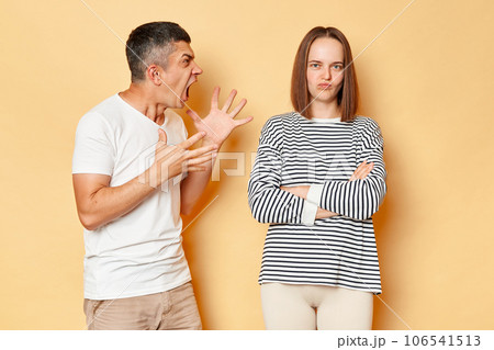 Crazy mad young man screaming with aggression arguing with brown haired woman in casual clothing standing isolated over beige background, having relationship problems. Crazy mad young man screaming with aggression arguing with brown haired woman in casual clothing standing isolated over beige background, having relationship problems. 106541513