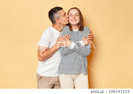 Loving romantic young couple man woman in casual clothing isolated over beige background expressing love husband hugging his wife and kissing. 106541529