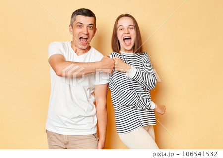 Excited laughing young couple friends man woman in casual clothing isolated over beige background making fist bump deal sreaming with happiness celebrating good idea. 106541532