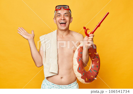 Extremely happy overjoyed adult man wearing shorts swimsuit snorkeling goggles holding donut rubber ring and bag isolated on yellow background enjoying summer recreation 106541734