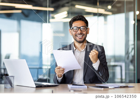Portrait of successful arab financier, experienced businessman smiling and looking at camera, holding financial report in hands, man satisfied with achievement results, triumph winner gesture. 106542350
