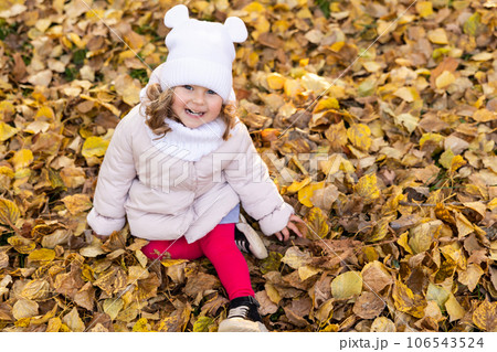 A cute pretty girl is running in the park in the middle of autumn leaves and smiling. 106543524