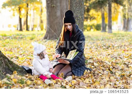 A mother is reading a book with her cute daughter while sitting on the lawn in the park 106543525