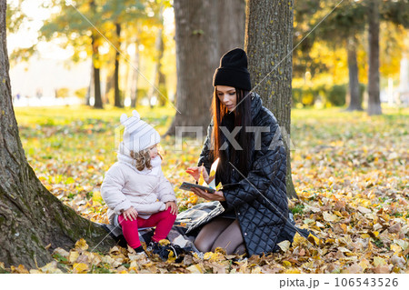 A mother is reading a book with her cute daughter while sitting on the lawn in the park 106543526