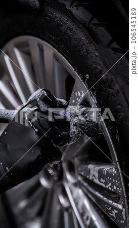 Employee of the car detailing studio or hand car wash thoroughly cleans an aluminum car wheel  106545189
