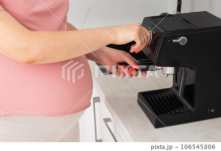 A pregnant girl with a big belly prepares coffee for the coffee machine. Benefits of coffee for pregnant women. A pregnant girl with a big belly prepares coffee for the coffee machine. Benefits of coffee for pregnant women. 106545806