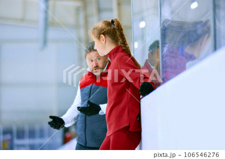 Teen girl, figure skating athlete in red sportswear standing with teach, sport coach and listening to techniques explanations Teen girl, figure skating athlete in red sportswear standing with teach, sport coach and listening to techniques explanations 106546276