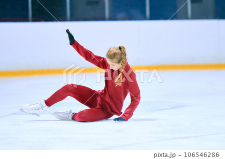 Challenges. Girl, figure skating athlete in red sportswear falling down during training on ice rink arena Challenges. Girl, figure skating athlete in red sportswear falling down during training on ice rink arena 106546286