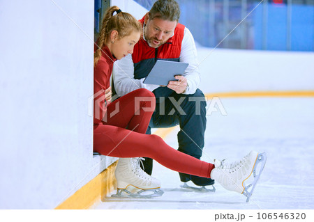 Girl, figure skating athlete with coach looking on tablet, learning techniques, watching videos on ice rink arena 106546320
