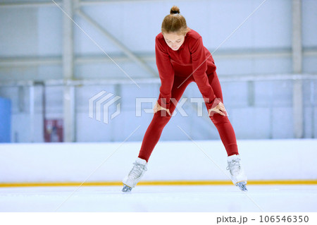 Girl in red sportswear, figure skating athlete standing on ice rink area and resting after hard training 106546350